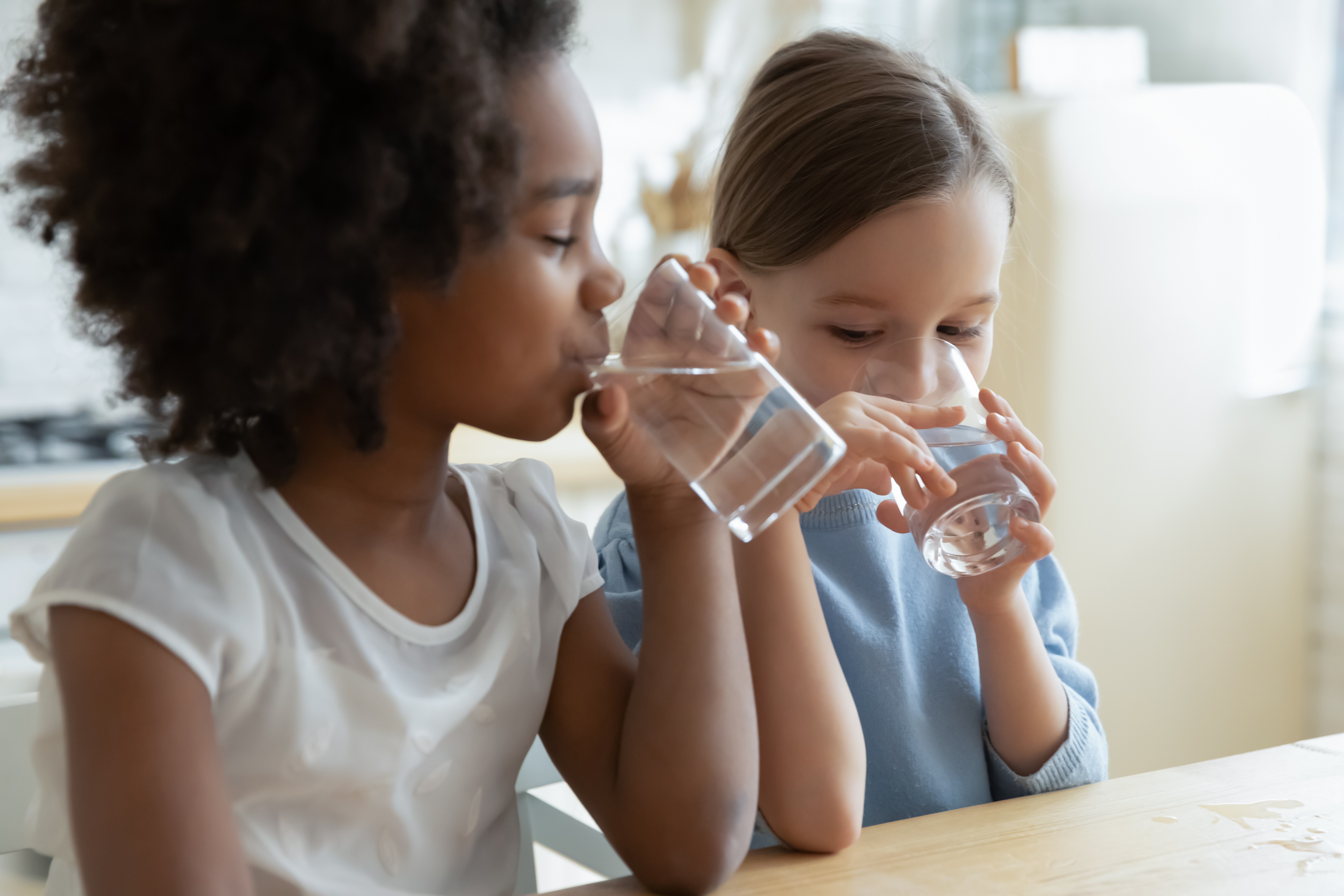 Two little girls drinking clear water from glasses