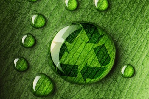 Water droplets on a green leaf, featuring a recycling symbol within one droplet, emphasizing sustainability and environmental conservation