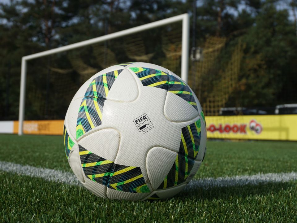 Voetbal met FIFA-logo op een grasveld, dichtbij een doel met een net op de achtergrond.