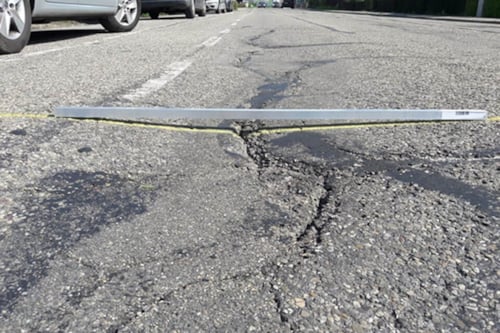 Een gebarsten asfaltweg met zichtbare scheuren en een meetinstrument dat over de scheuren is geplaatst