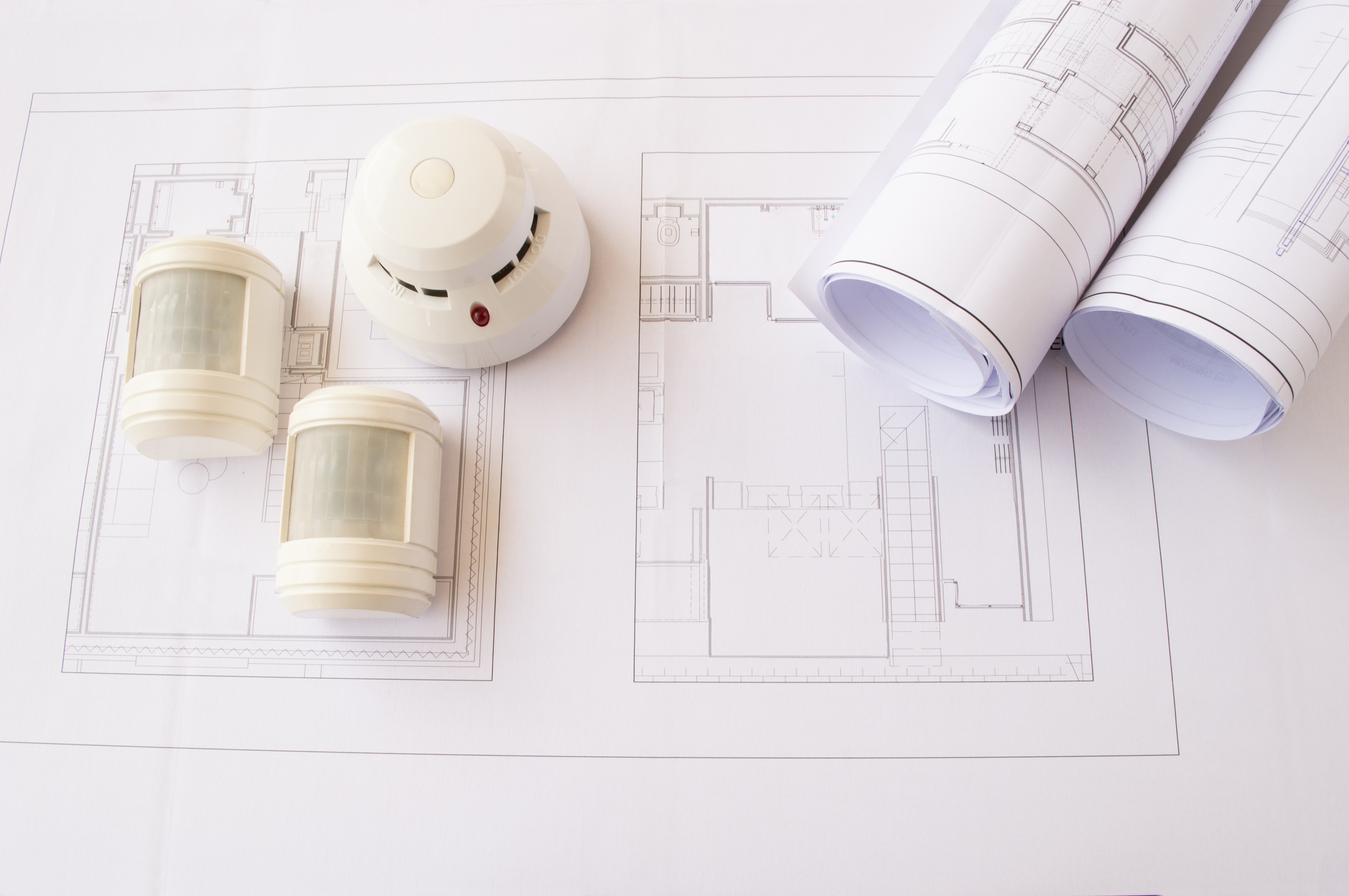 Roluimtekeningen met opgerolde bouwplannen, een rookmelder en twee bewegingssensoren.