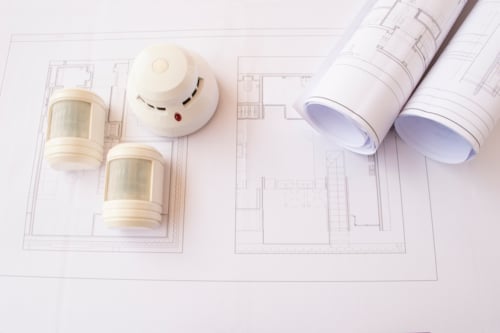 Roluimtekeningen met opgerolde bouwplannen, een rookmelder en twee bewegingssensoren.