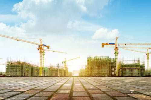 Bouwplaats met meerdere torenkranen en gebouwen in aanbouw, onder een blauwe lucht met witte wolken.