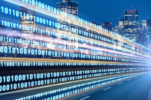 Verlichte skyline van een stad bij nacht met een snelweg waarop grafische binaire gegevens (nullen en enen) zijn geprojecteerd.