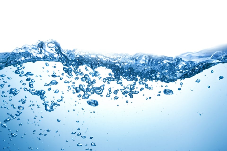 A close-up of water with bubbles, showcasing a clear blue surface and a bright white background.