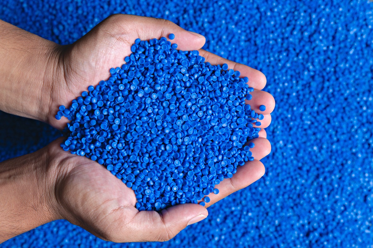 Hands holding blue plastic pellets over a background of blue granules.