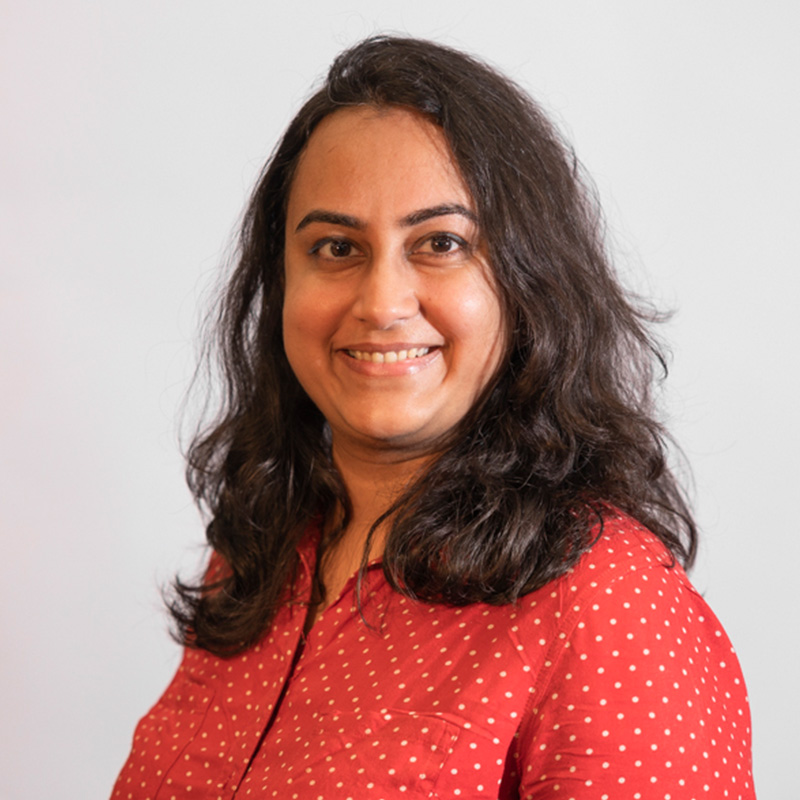 Rashi Mor, with long dark hair, smiling and wearing a red polka dot shirt, posing against a plain background