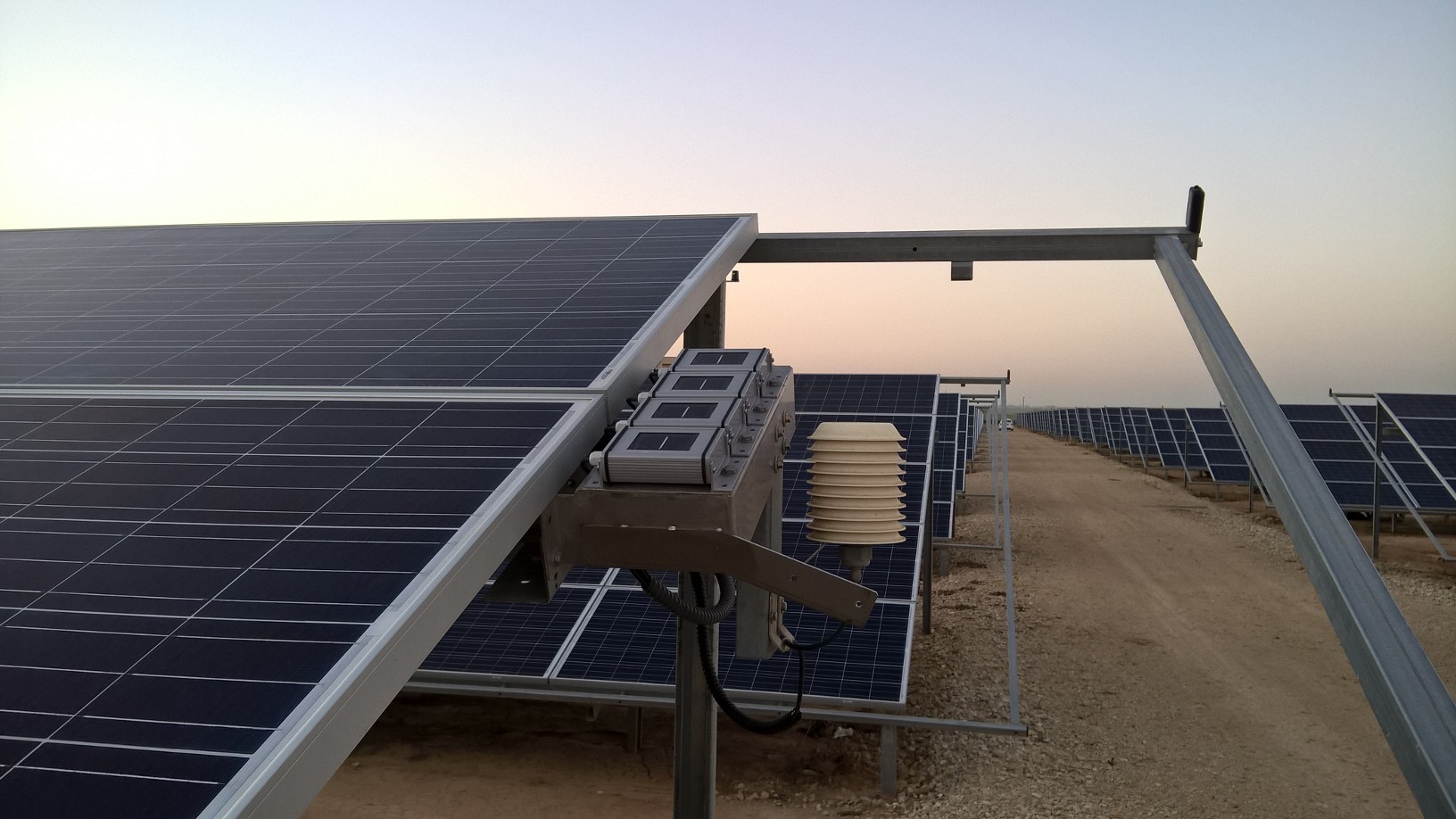 Solar panels in a desert landscape, mounted on metal frames, with an early morning sky