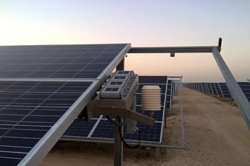 Solar panels in a desert landscape, mounted on metal frames, with an early morning sky