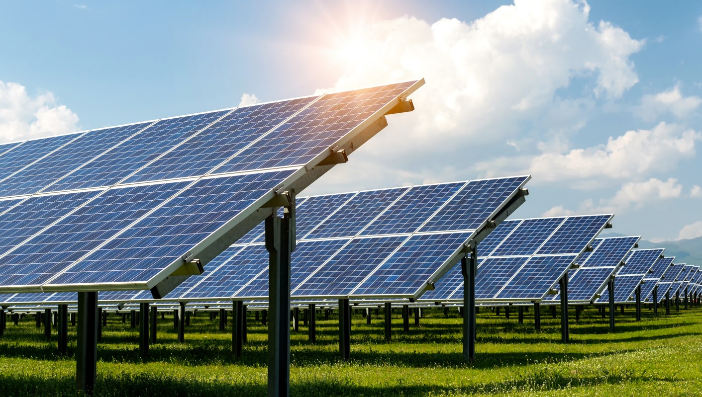 Paneles solares instalados en un campo verde bajo un cielo soleado y parcialmente nublado.