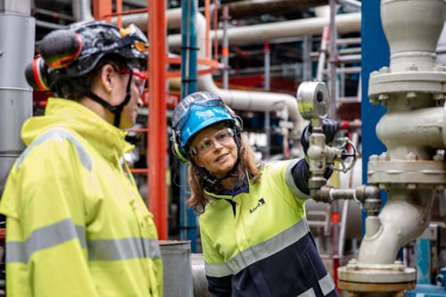 Två besiktningsingenjörer från Kiwa i skyddskläder arbetar vid rör och ventiler i en industriell miljö.