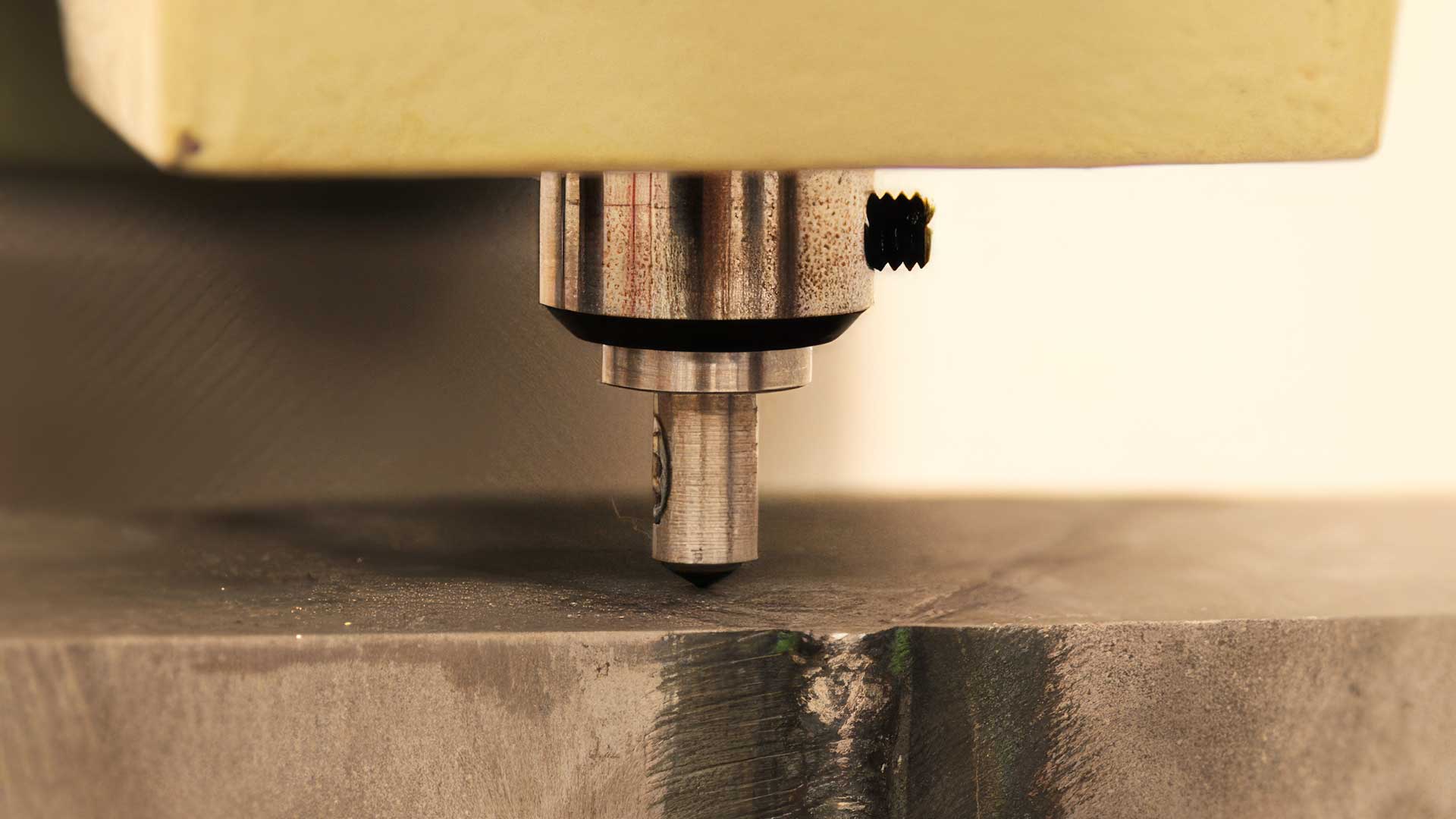 Närbild av en maskin som utför hårdhetsmätning där ett verktyg pressas mot en metallbit.