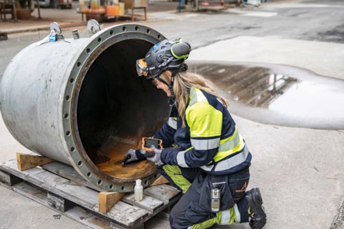 Inspektör i arbetskläder undersöker insidan av ett stort metallrör på en industriplats.