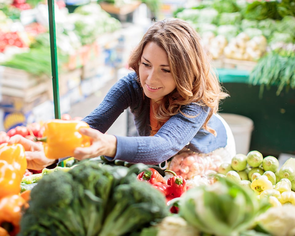 En kvinna plockar grönsaker på ett grönsaksstånd. 