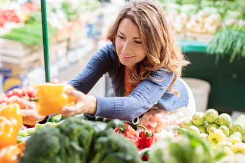En kvinna plockar grönsaker på ett grönsaksstånd.