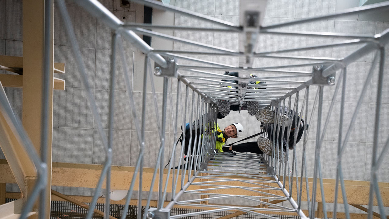 Män med skydds- och fallskyddsutrustninghar klättrat upp i en mast och tittar ner. 