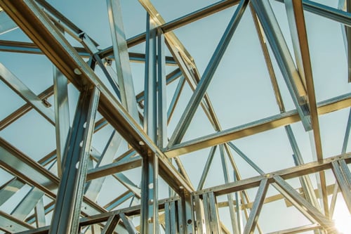 Solen reflekterar mot blänkande stålramar av en byggkonstruktion med blå himmel i bakgrunden.