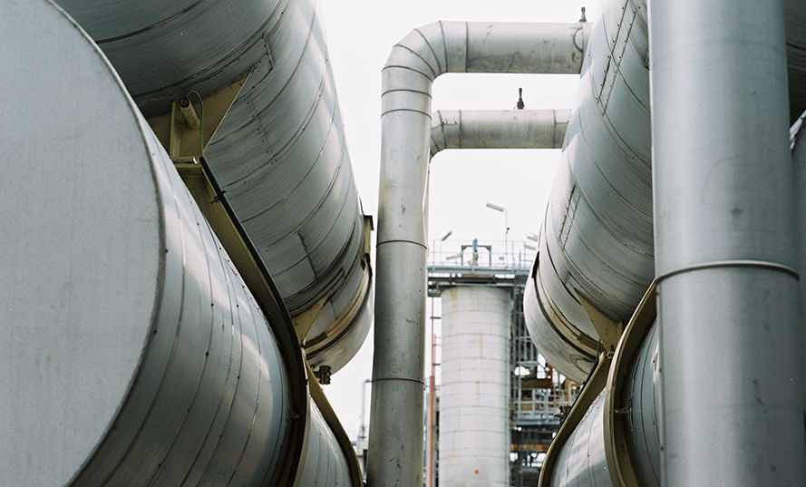 Industriella rör och cylindrar av metall med en fabriksmiljö i bakgrunden.