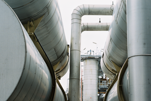 Industriella rör och cylindrar av metall med en fabriksmiljö i bakgrunden.