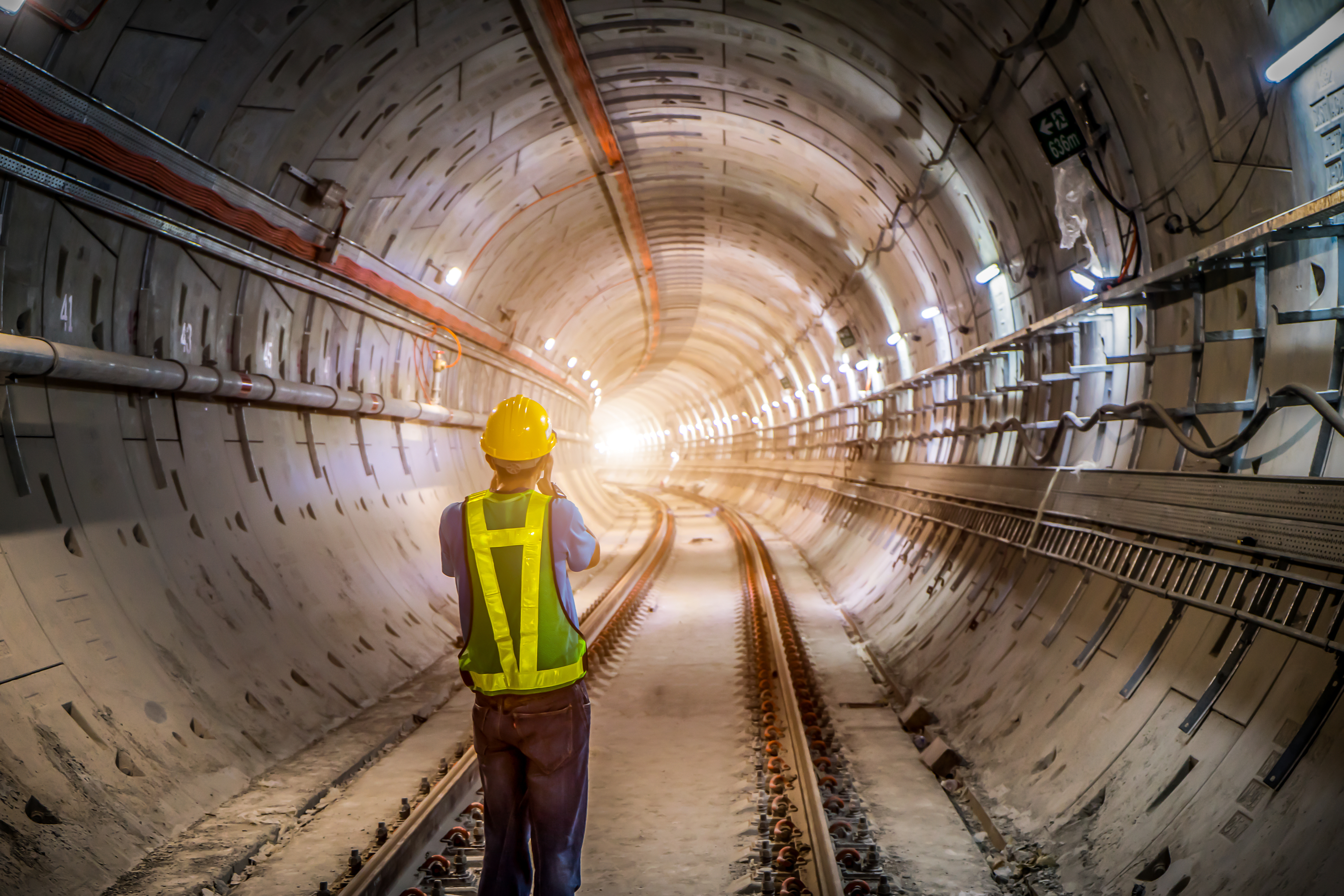 Kiwa engineer wearing a hard hat and safety vest standing inside an illuminated subway tunnel construction site.