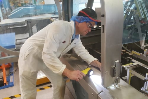 Kiwa auditor in protective gear inspecting machinery in a factory setting with a flashlight