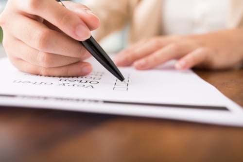 Person filling out a checklist with a black pen on a white paper form, focusing on decision-making or survey completion