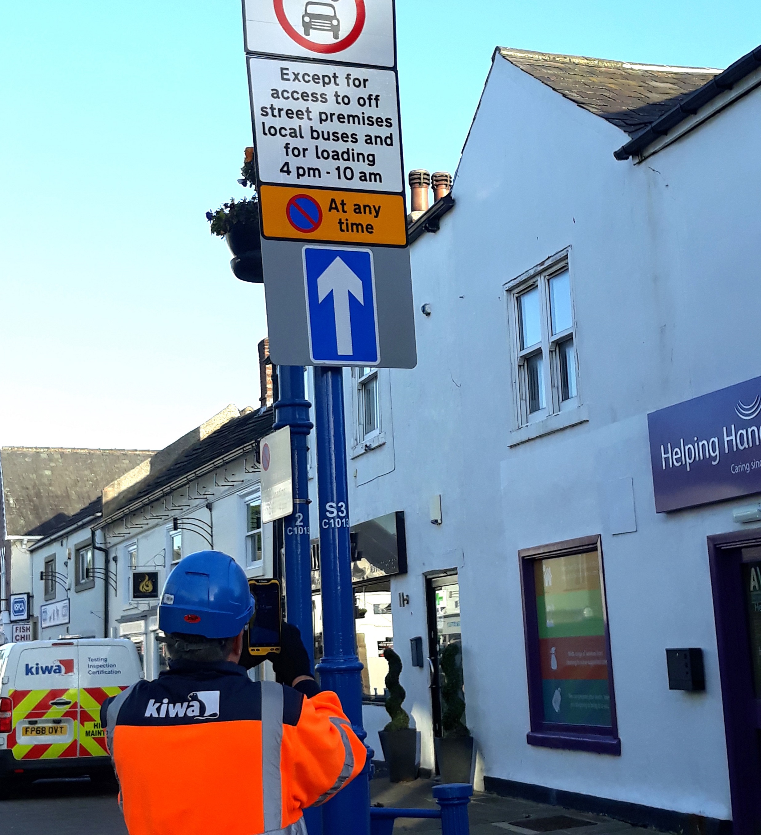 Kiwa employee inspecting street sign in urban area with one-way traffic and parking restrictions, featuring nearby buildings and service van