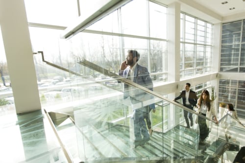 Business professionals walking up a modern glass staircase in a bright office building