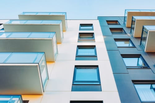 Modern apartment building with glass balconies and blue windows against a clear sky
