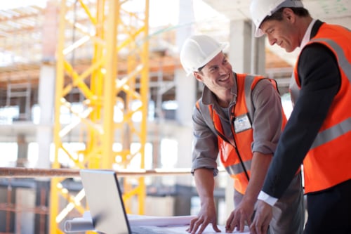 Construction workers in safety vests and helmets discussing blueprints at a building site