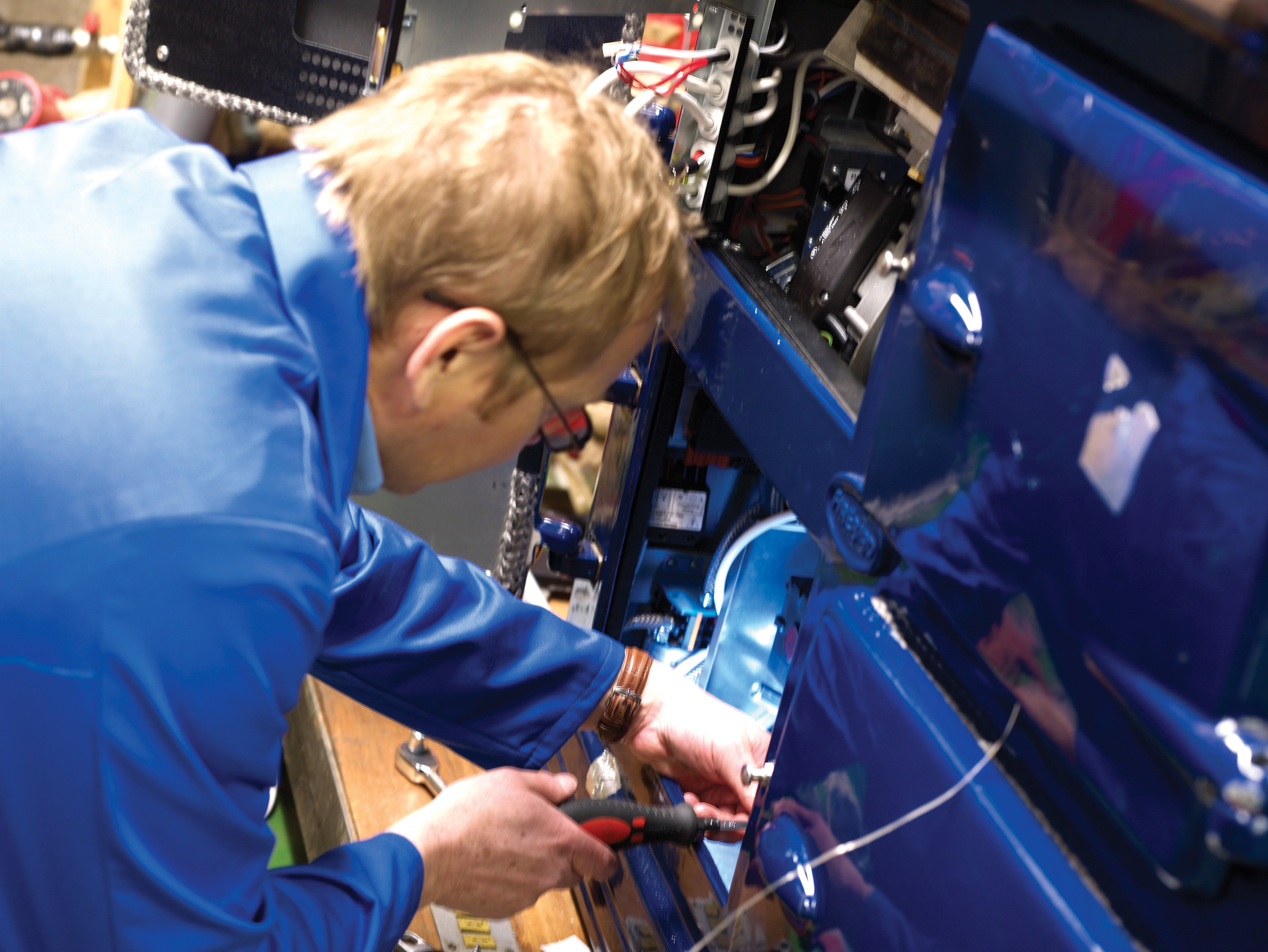 Technician repairing machinery in a workshop, focused on electrical components and wiring