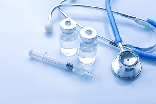 Syringe and two medicine vials next to a stethoscope on a reflective blue surface, representing healthcare and medical supplies