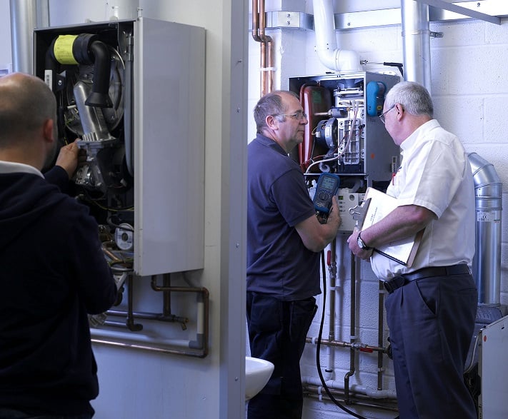 Kiwa trainer and student are inspecting a heating system in a utility room, examining complex piping and machinery