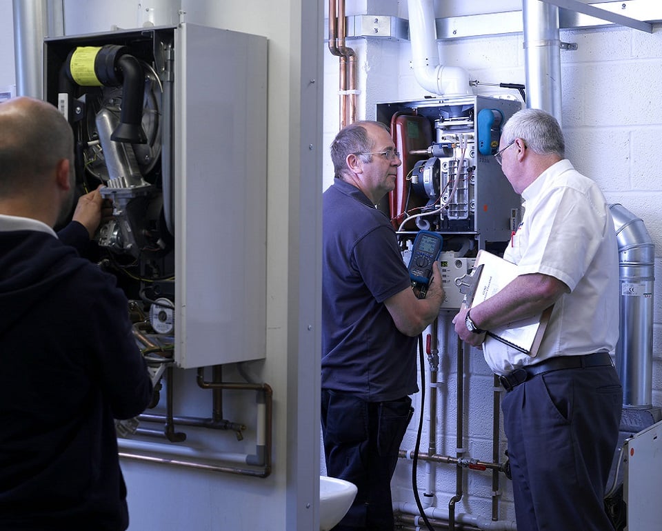 Kiwa trainer and student inspecting and repairing a gas boiler in a utility room, demonstrating boiler maintenance and troubleshooting
