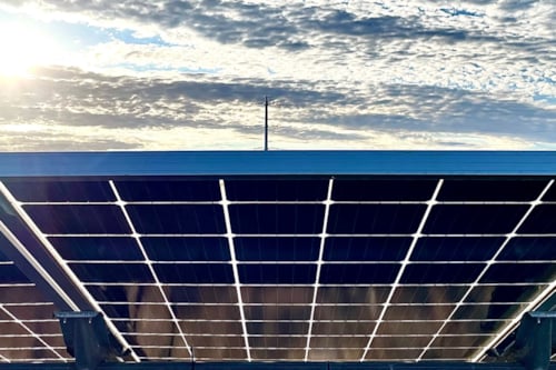 Solar panels on a rooftop under a bright sky with scattered clouds