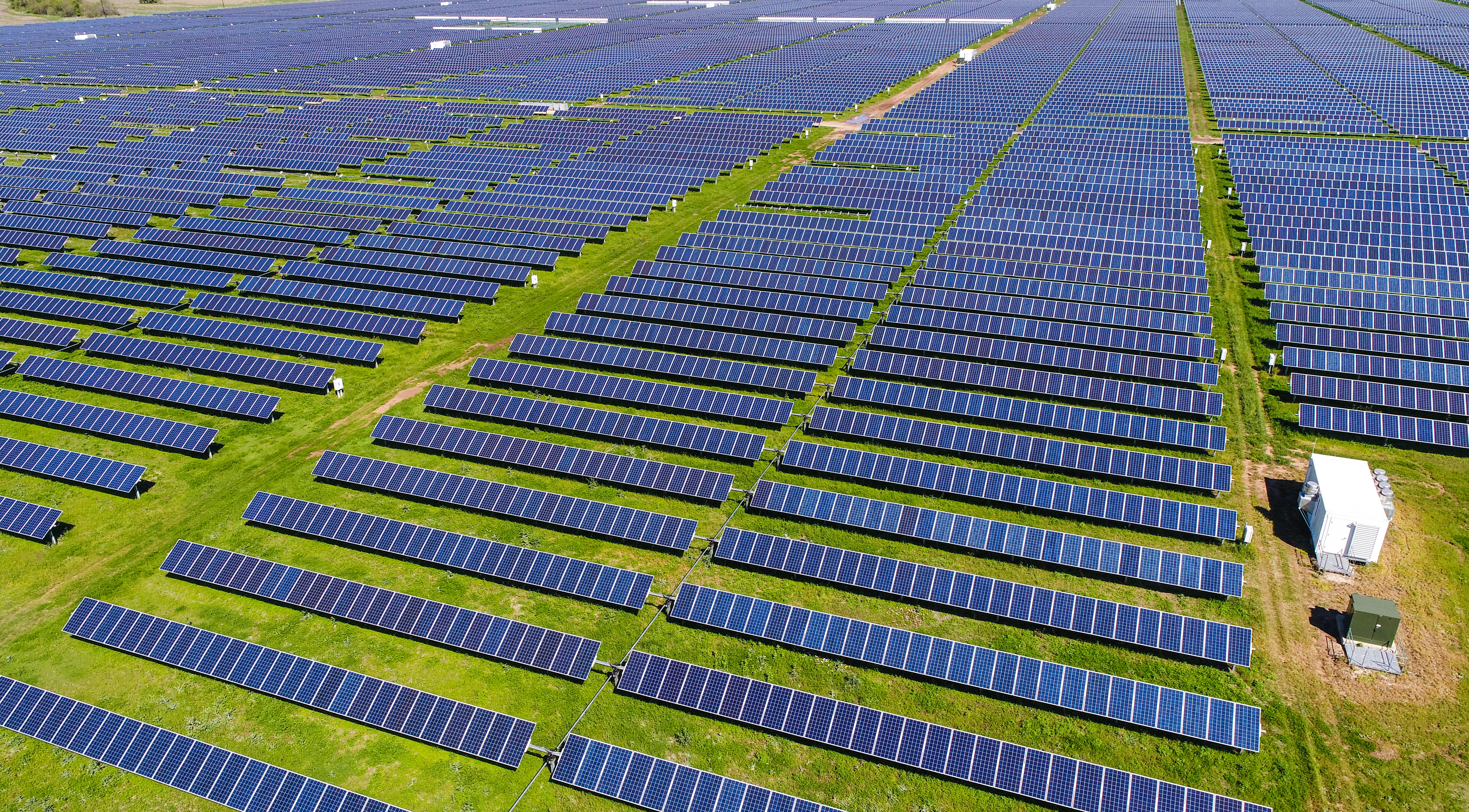 Aerial view of a solar farm featuring rows of blue solar panels on a green landscape, illustrating renewable energy technology